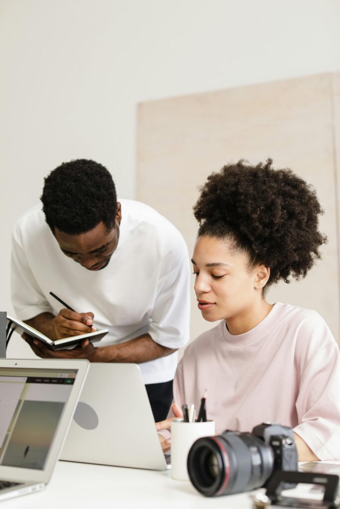 Two colleagues collaborate in a creative workspace with laptops and camera.